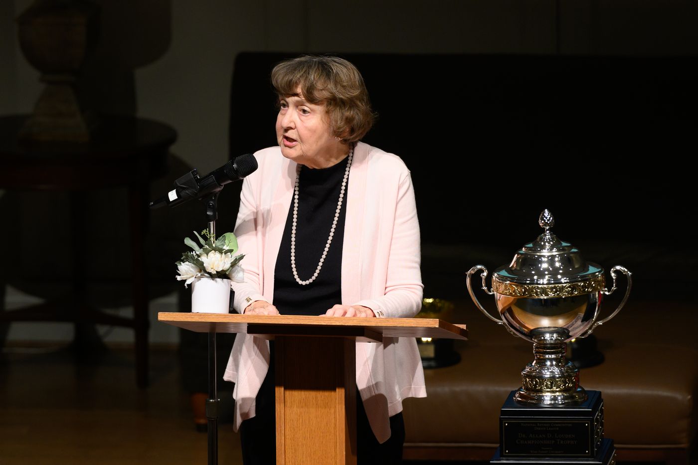 A debater in a pink cardigan and pearls speaks at the podium.