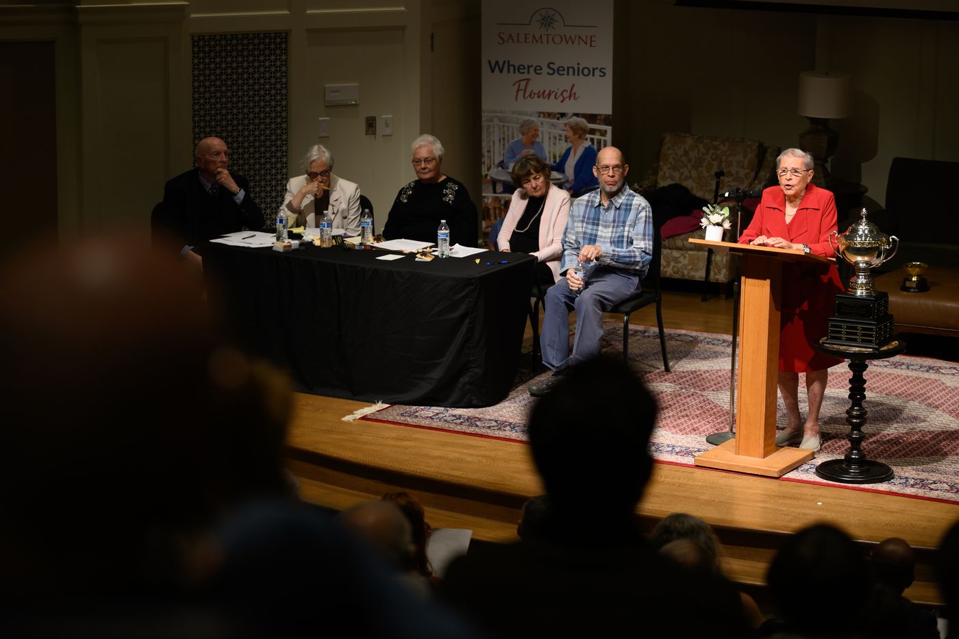 View from the audience of a debater at the podium, with her team seated behind her.
